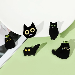 Detail view of 5 cute black cat enamel pins set on a white ceramic plate background