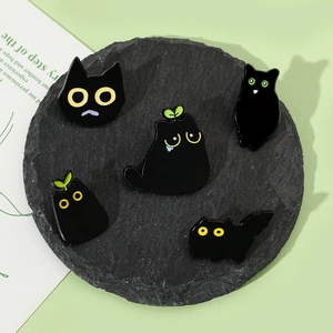 Detail of five cute black cat enamel pins with cartoon expressions on a stone plate