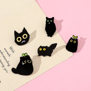 Detail view of five cute black cartoon cat enamel pins with yellow eyes on pink backdrop