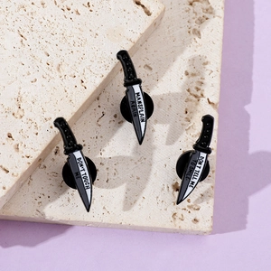 Detailed macro view of three feminist dagger enamel pins on a textured stone display