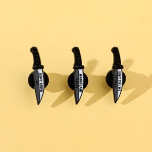 Detail of three black and white enamel dagger pins with feminist slogans on yellow backdrop