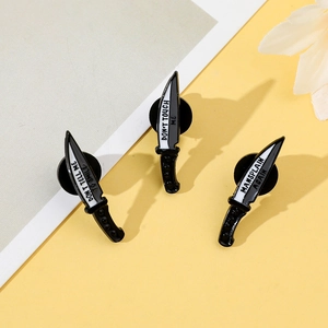 Three black dagger enamel pins with feminist slogans on yellow and gray background