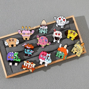 Detail of assorted cartoon monster food enamel pins on a velvet jewelry display tray