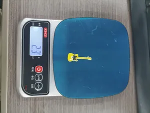 Detailed view of a yellow electric guitar enamel charm on an electronic scale showing 2.3g