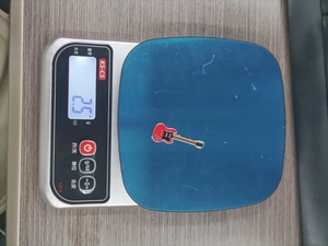 Macro view of a 2.5g red electric guitar enamel pin being weighed on a digital scale