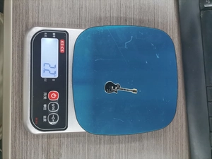 Detailed view of metal guitar badge weighing 2.2 grams on an electronic scale