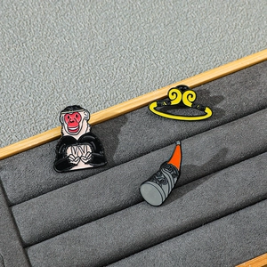 Macro shot of cartoon Monkey King enamel pins and golden hoop set on a jewelry tray