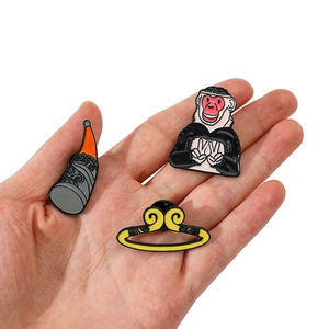 Detailed close-up of three enamel Monkey King pins held by hand on white background