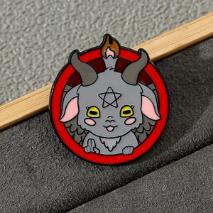 Detail of a round Baphomet enamel pin with red border and grey ram head on grey fabric
