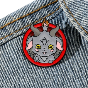 Cartoon Baphomet enamel pin with red circle and pentagram on blue denim fabric