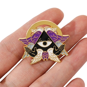 Macro shot of mystic triangle enamel pin with purple wings and eye detail held by hand