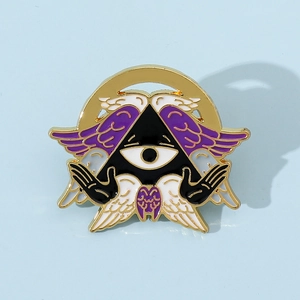 Macro detail of enamel pin featuring a golden all-seeing eye with purple wings design