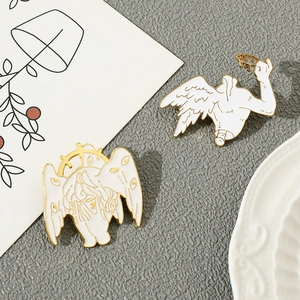 Detail of Cthulhu angel enamel pins with white wings and gold outlines on a textured surface