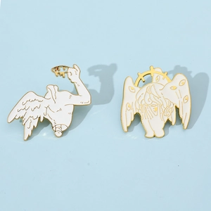 Detailed view of surreal white enamel pins with gold trim and multi-eyed angel wings
