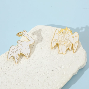 Macro view of gold-trimmed white enamel seraphim pins on a textured stone surface