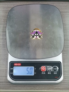 Detail shot of a Cthulhu angel enamel pin on a digital scale weighing 5.0 grams