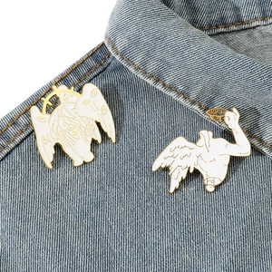 Surreal white enamel angel pins set with gold trim on blue denim fabric background