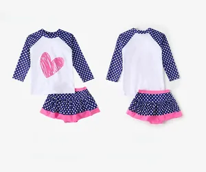 Flat lay of polka dot long sleeve swim top and skirt for girls with heart print detail
