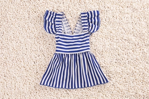 Flat lay of navy blue and white striped toddler swimsuit with ruffle details on pebbles