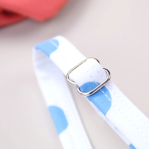 Detail of adjustable metal buckle and blue polka dot strap on white kids' swimwear