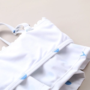 Detail of white swimsuit fabric featuring light blue polka dots and ruffle edges