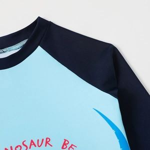 Detail of baby boy dinosaur swimsuit showing blue raglan sleeves and quality stitching