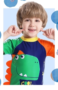 Detailansicht der Jungen-Badebekleidung mit grünem Dinosaurier-Druck und COOL-Schriftzug