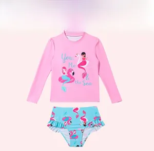 Flat lay of pink long-sleeved girls' rash guard set with flamingo and mermaid prints