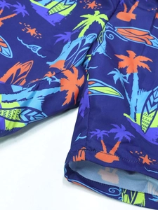 Detail of boys beach shorts with tropical palm trees and surfboard patterns in dark blue