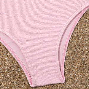 Bikini a coste rosa per bambine con gonna presentato su sfondo di sabbia marina