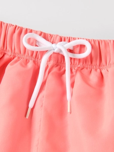 Detail der Badeshorts für Jungen mit elastischem Bund, weißem Kordelzug und korallenfarbenem Stoff