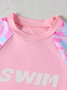 Detail of pink girls' short sleeve swimwear showing white SWIM letters and floral print