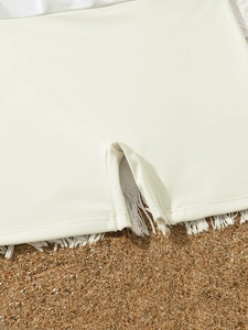 Detalle de los pantalones de baño color crema para niñas con flecos en la arena