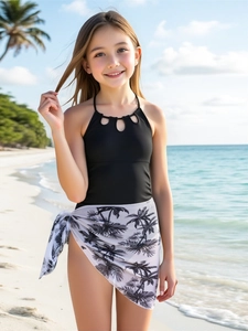 Detail eines schwarzen Mädchen-Badeanzugs mit Palmen-Sarong an einem sonnigen Strand