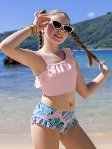Detail of pink ruffled swim top and tropical leaf print bottoms on a sunny beach