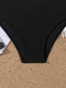 Close-up of black ribbed girls' bikini bottoms on beach sand with soft natural lighting