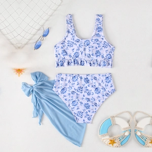 Three-piece girls floral bikini set with blue mesh sarong on a summer beach background