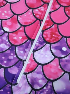 Macro detail of mermaid scale print swimwear fabric with white zipper and precise stitching