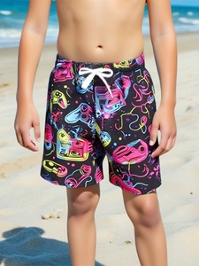 Detail of boys quick dry swim shorts with neon gaming pattern on a sandy beach