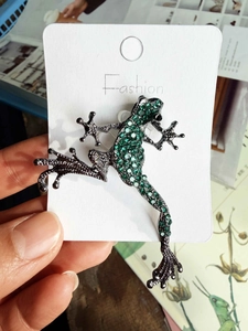 Detail of the green rhinestone frog brooch in antique copper finish on a display card
