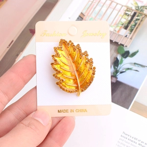 Dettaglio di una spilla a foglia dorata con smalto giallo e strass arancioni