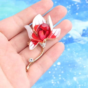 Handheld view of a floral enamel brooch with red crystal and gold plating