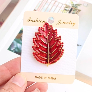 Dettaglio macro di spilla a foglia in smalto rosso con strass su carta regalo