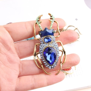 Macro shot of beetle brooch featuring blue crystals and teardrop gemstone on golden alloy
