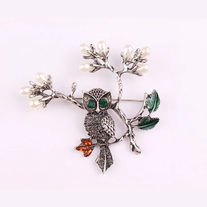 Vue macro d'une broche hibou avec yeux en cristal vert, perles blanches et feuilles