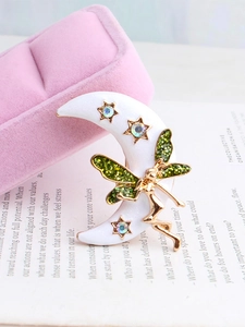 Détail macro d'une broche fée lune avec croissant blanc, ailes pailletées vertes et strass
