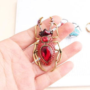 Detailed view of a vintage beetle brooch with red rhinestones held by a hand
