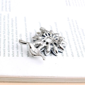 Silver flower brooch with blue petals and secure pin clasp on vintage book background