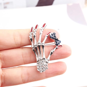Close-up of skeleton hand brooch with blue crystal bow and red enamel fingertips