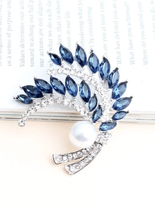 Dettaglio macro della spilla a spiga con strass blu e una perla bianca su un libro